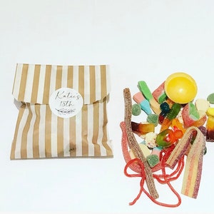 May include: A brown and white striped paper bag with a white circle sticker that says "Katie's 18th" on it. A pile of colorful gummy candies is next to the bag.