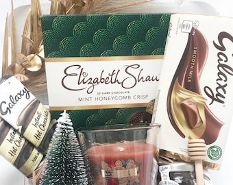 May include: A gift box filled with treats, including a box of Elizabeth Shaw dark chocolate mint honeycomb crisp, Galaxy chocolate, a gingerbread-scented candle, and a jar of honey. Decorative gold-colored foliage adds a festive touch.