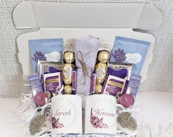 May include: A gift basket filled with lavender-themed bath and body products, including a bath towel, bath bombs, a pillow spray, and two mugs with the names "Sarah" and "Hassan" printed on them.