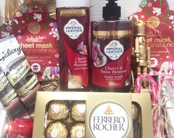 May include: A gift basket with skincare products, chocolates, and hot chocolate. The basket includes Imperial Leather Cherry & Snow Blossom body wash and hand wash, sheet masks, Ferrero Rocher chocolates, and candy canes. The products are arranged with decorative elements.