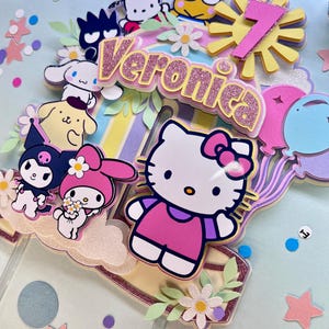 May include: A colorful cake topper featuring Hello Kitty, My Melody, and other cartoon characters. The topper includes a pink and yellow sun with the number 7, a pink and white banner with the name Veronica, and a variety of flowers and leaves.
