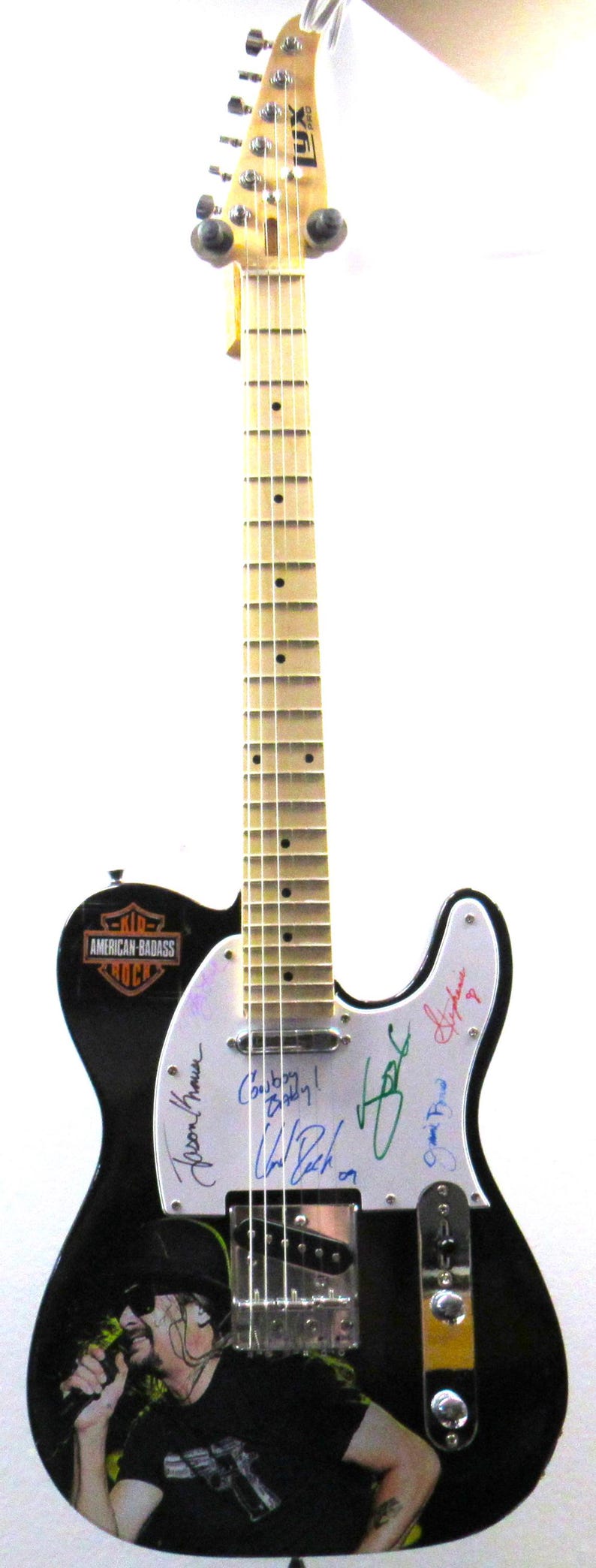 K&ouml;nnte beinhalten: Schwarze E-Gitarre mit wei&szlig;em Schlagbrett, mit einer Grafik eines K&uuml;nstlers und Unterschriften. Die Gitarre hat den Text "AMERICAN-BADASS ROCK" und "LUX PRO" auf der Kopfplatte.