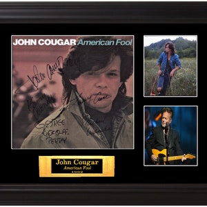 Puede incluir: Un collage de fotos enmarcado con una portada de álbum firmada de "American Fool" de John Cougar, una foto de John Cougar en un campo y una foto de John Cougar actuando en el escenario con una guitarra.