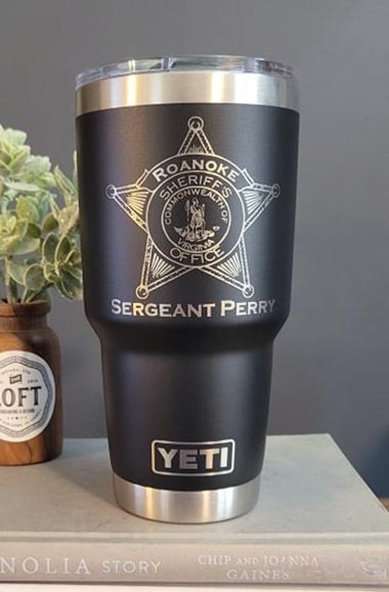 May include: A black Yeti tumbler with a silver lid and base. It has a laser engraved design of a star with the words "Roanoke Sheriffs Commonwealth of Virginia Office" and "Sergeant Perry".
