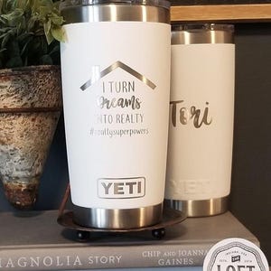May include: Two white Yeti tumblers with silver accents. One tumbler has the text "I TURN Dreams INTO REALTY #realtysuperpowers" and the Yeti logo. The other tumbler is inscribed with the name "Tori".