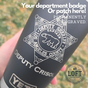 May include: A black Yeti tumbler with a silver engraved Los Angeles County Sheriff's Department badge, a bear, and the words "DEPUTY SHERIFF CAPTAIN" and "DEPUTY CRISOL". The text "PERMANENTLY ENGRAVED" is also engraved on the tumbler.