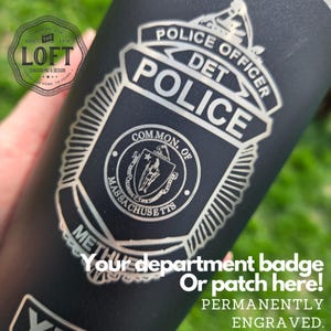 May include: Black tumbler with a silver police badge design. The badge includes the words "Police Officer Det Police" and "Common. of Massachusetts." The text "Your department badge or patch here! Permanently engraved" is also visible.