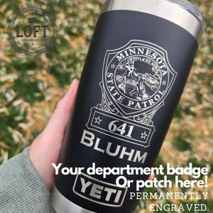 May include: A black Yeti tumbler with a silver lid and a laser engraved Minnesota State Patrol badge with the number 641 and the name Bluhm. The text "Your department badge or patch here! Permanently engraved." is also engraved on the tumbler.