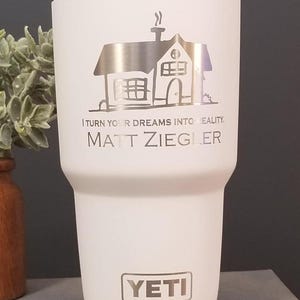 May include: A white Yeti tumbler with a silver lid and base. The tumbler features a silver illustration of a house and the text "I TURN YOUR DREAMS INTO REALITY. MATT ZIEGLER." The Yeti logo is also visible.