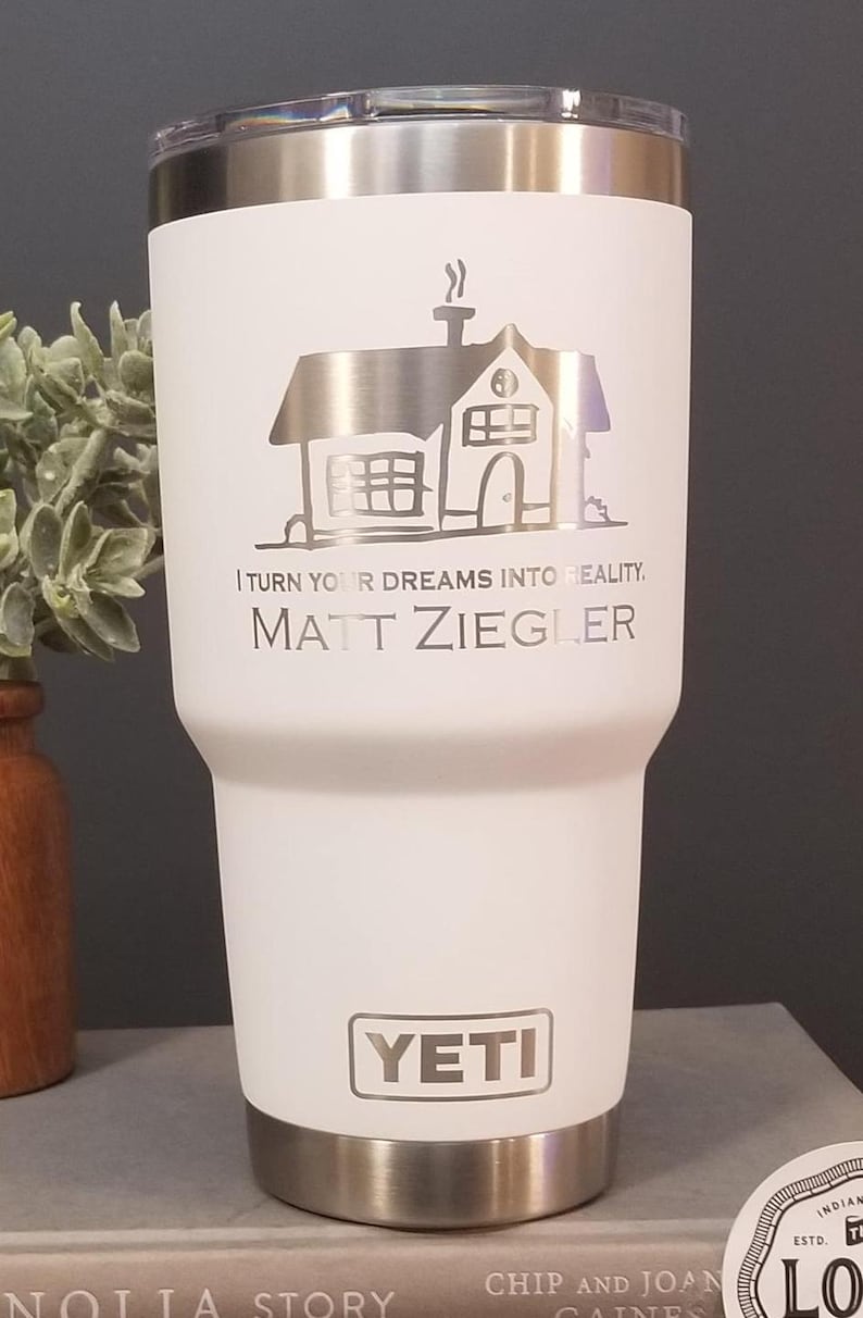 May include: A white Yeti tumbler with a silver lid and base. The tumbler features a silver illustration of a house and the text "I TURN YOUR DREAMS INTO REALITY. MATT ZIEGLER." The Yeti logo is also visible.