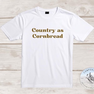 Puede incluir: Una taza de cerámica blanca con un asa negra y el texto "But First, Coffee" en negro, con una fuente de estilo manuscrito. La taza está sobre una superficie blanca.