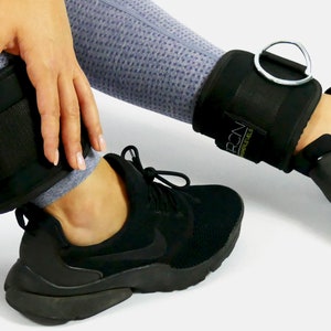 Könnte beinhalten: Ein Paar schwarze Fußgewichte mit verstellbaren Riemen und einem Metallring. Die Gewichte sind mit "PRCN" und "HIGH-LEVELS" beschriftet.