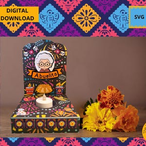 May include: A Day of the Dead altar featuring the word "Abuelita" and a cartoon image of a grandmother. The altar is black with colourful designs and a small candle. Marigold flowers are next to the altar. The words "Digital Download" and "SVG" are also visible.
