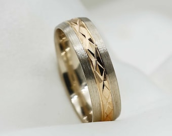 May include: A two-tone ring featuring a brushed silver-colored band with a central inlay of polished gold-colored metal. The gold-colored section displays a repeating geometric diamond-cut pattern that catches the light across its surface.