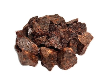 May include: A close-up of a pile of dark brown, irregularly shaped pieces of dried fruit. The fruit has a slightly shiny surface and appears to be quite hard.