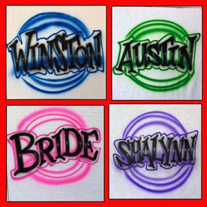 Peut inclure: Quatre t-shirts blancs avec des noms diff&eacute;rents peints &agrave; l'a&eacute;rographe dans des cercles color&eacute;s. Les noms sont Winston, Austin, Bride et Shalyann.