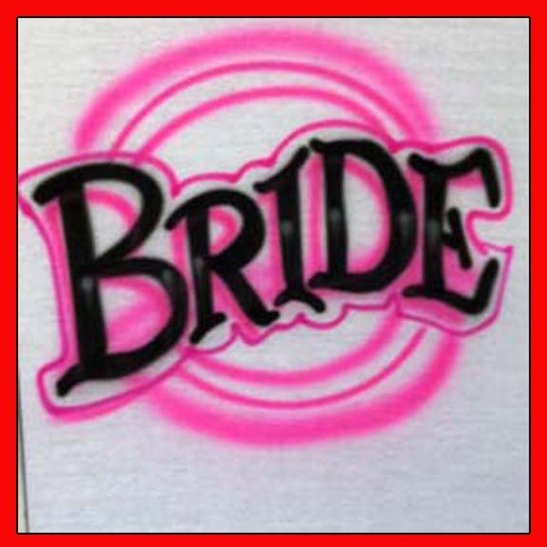 Peut inclure: Un t-shirt blanc avec un motif airbrush rose du mot "BRIDE" en lettres noires.