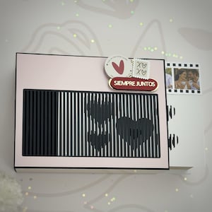 Puede incluir: Una caja decorativa rosa y negra con un diseño de corazón y las palabras "SIEMPRE JUNTOS". La caja tiene una foto de una pareja y un diseño de sello con corazones y XOXO. Un regalo romántico.