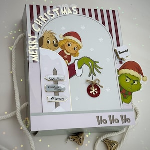 Puede incluir: Una caja de regalo con temática navideña con un diseño a rayas blancas y rojas. La caja presenta ilustraciones de personajes con gorros de Papá Noel, copos de nieve y el texto "Merry Christmas" y "Ho Ho Ho". Incluye un asa de cuerda blanca.