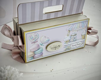 May include: A decorative gift box with a handle and a pink ribbon. The box features illustrations of sweets, including lollipops, macarons, and an ice cream cart. The text "Sweet Treats" is visible on the box.