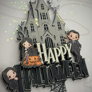 Może przedstawiać: Wielowarstwowa dekoracja na tort przedstawiająca szary nawiedzony dom, białego ducha i trzy postacie z kreskówek. Napis brzmi HAPPY HALLOWEEN złotymi i czarnymi literami. Projekt zawiera czarną pajęczynę, pająka oraz pomarańczową dynię.
