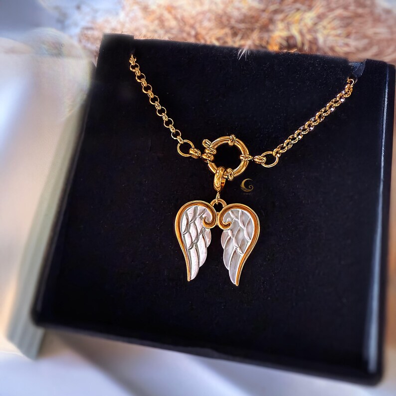 Waterproof angel wings necklace on black jewelry box, highlighting shiny gold chain and silver wings pendant.