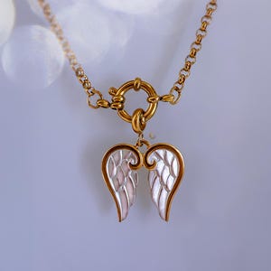 Close-up of angel wings pendant with toggle clasp in focus, showing elegant contrast between gold edges and silver fill.