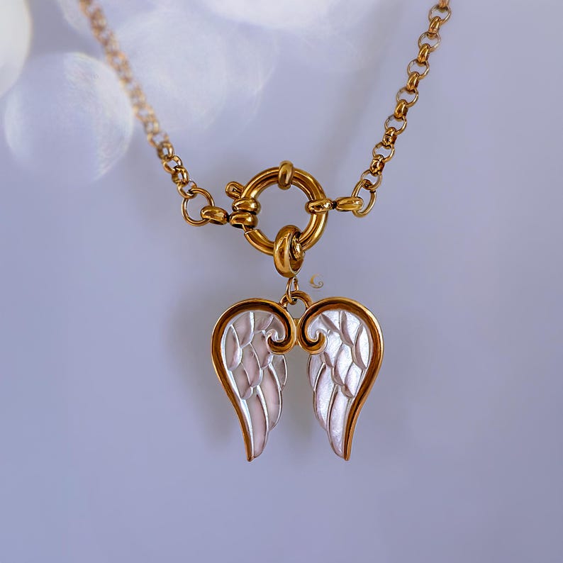 Close-up of angel wings pendant with toggle clasp in focus, showing elegant contrast between gold edges and silver fill.