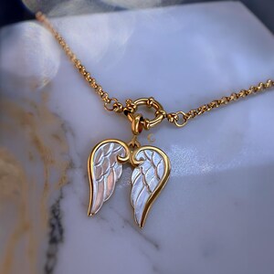 Gold angel wings necklace displayed on black jewelry box, showing luminous silver enamel wings and round toggle clasp.