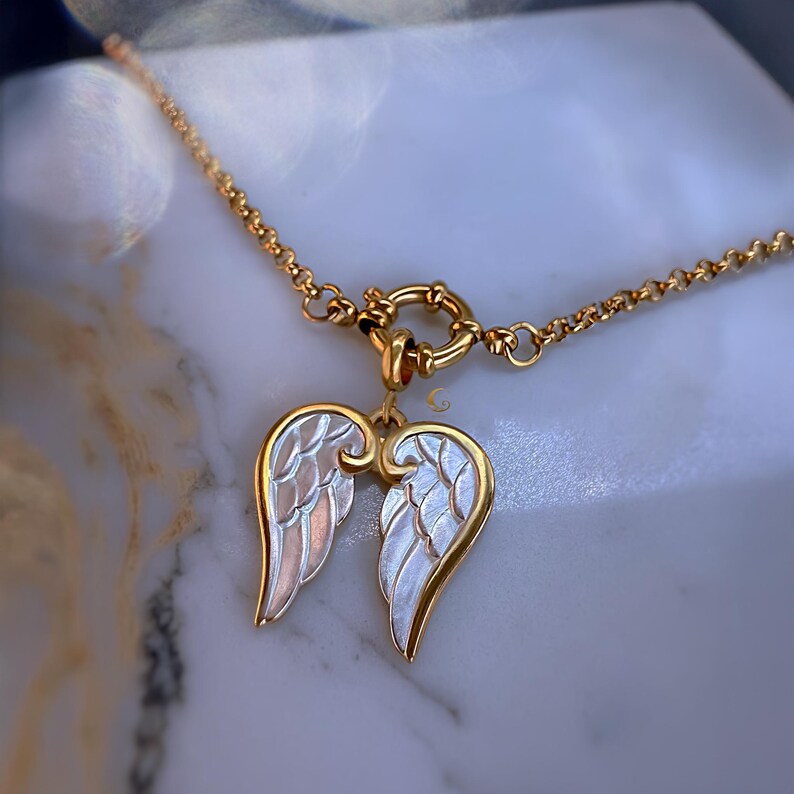 Gold angel wings necklace displayed on black jewelry box, showing luminous silver enamel wings and round toggle clasp.