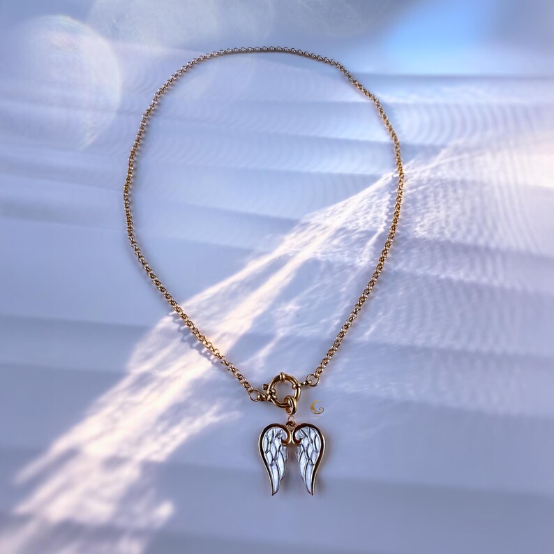 Full view of angel wings necklace arranged in a circle on stone-textured background, showing clasp and pendant placement.
