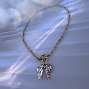 Full view of angel wings necklace arranged in circle on bright marble-like background, showing pendant and waterproof gold chain.