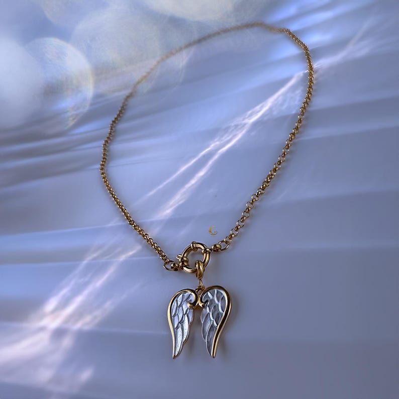 Full view of angel wings necklace arranged in circle on bright marble-like background, showing pendant and waterproof gold chain.