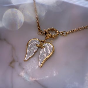Close-up of angel wings pendant resting on stone-textured white surface, glowing softly in daylight.