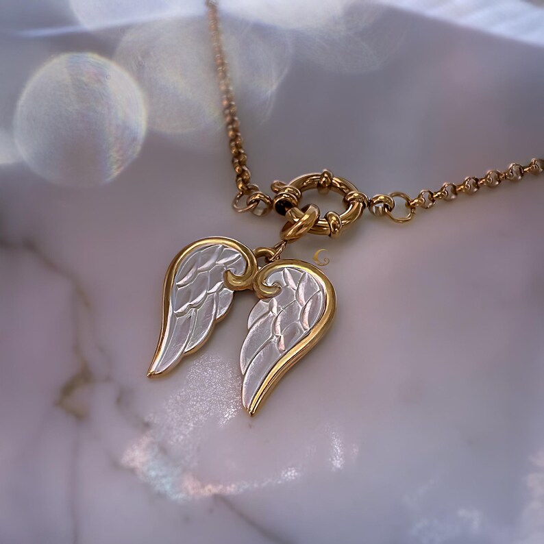 Close-up of angel wings pendant resting on stone-textured white surface, glowing softly in daylight.