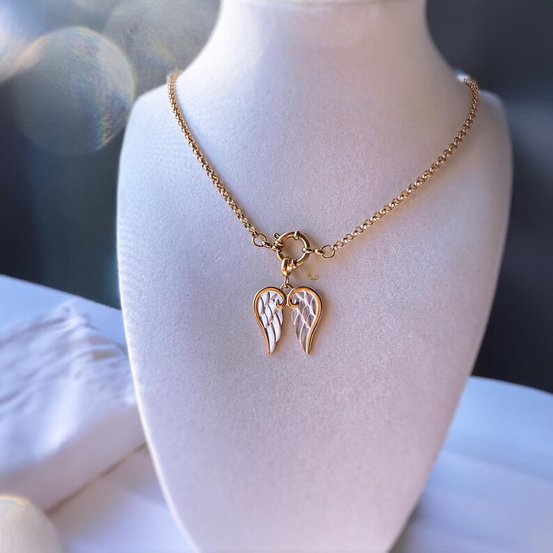 Gold angel wings necklace displayed on white jewelry bust, simple minimal setup emphasizing pendant’s shine.