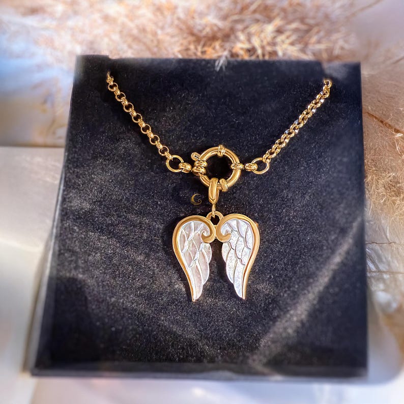 Gold angel wings necklace on model’s neck, elegant close-up emphasizing reflective shine of 18K gold plating.