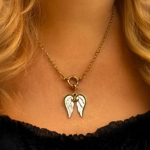 Gold angel wings necklace on model’s neck, elegant close-up emphasizing reflective shine of 18K gold plating.