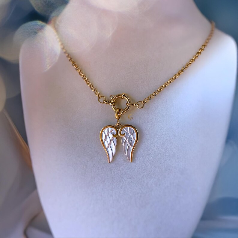 Gold and silver angel wing necklace displayed on jewelry bust, showing detailed wing engraving and toggle clasp.