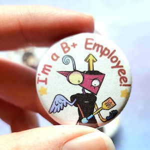 K&ouml;nnte beinhalten: Ein runder Button mit dem Text "I'm a B+ Employee!" zeigt einen Cartoon-Roboter mit einem rosa Kopf, schwarzem K&ouml;rper und gelbem Spatel. Der Roboter hat einen blauen Fl&uuml;gel und einen gelben Stern.