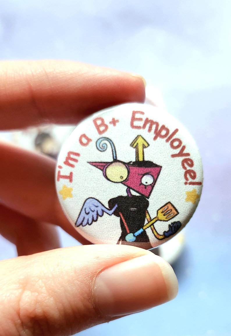 K&ouml;nnte beinhalten: Ein runder Button mit dem Text "I'm a B+ Employee!" zeigt einen Cartoon-Roboter mit einem rosa Kopf, schwarzem K&ouml;rper und gelbem Spatel. Der Roboter hat einen blauen Fl&uuml;gel und einen gelben Stern.