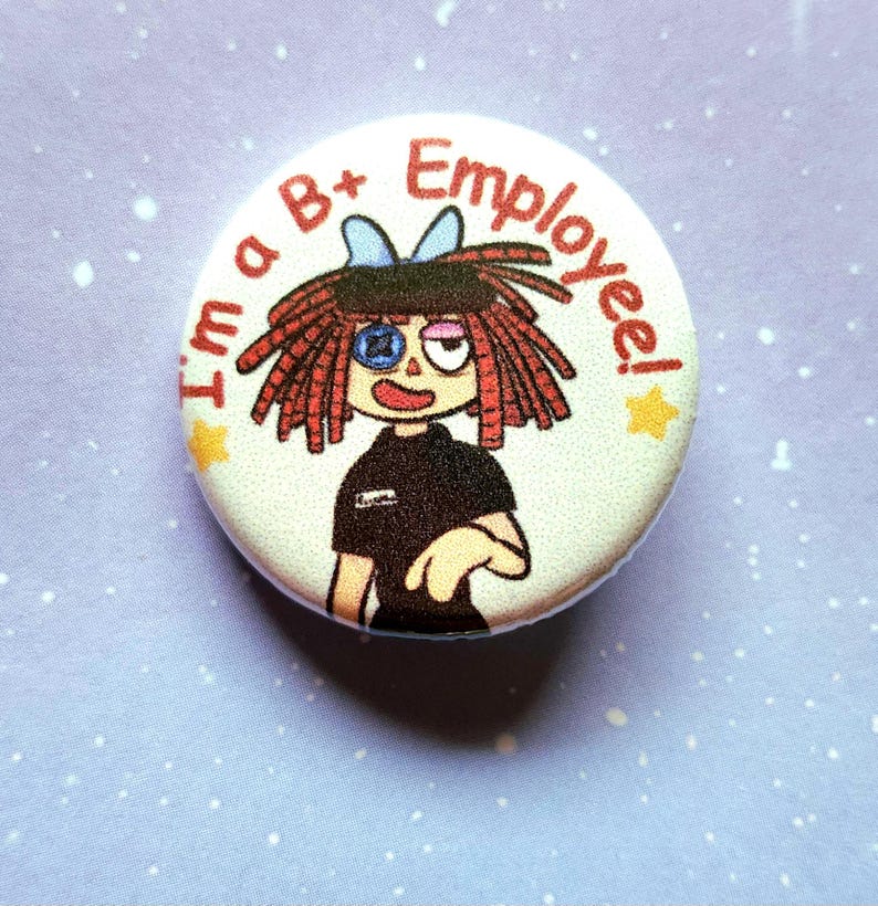 K&ouml;nnte beinhalten: Ein runder Button mit einer Cartoon-Illustration einer Person mit roten Haaren und dem Text "I'm a B+ Employee!" in Rot. Die Figur hat ein schwarzes Hemd und eine blaue Schleife.
