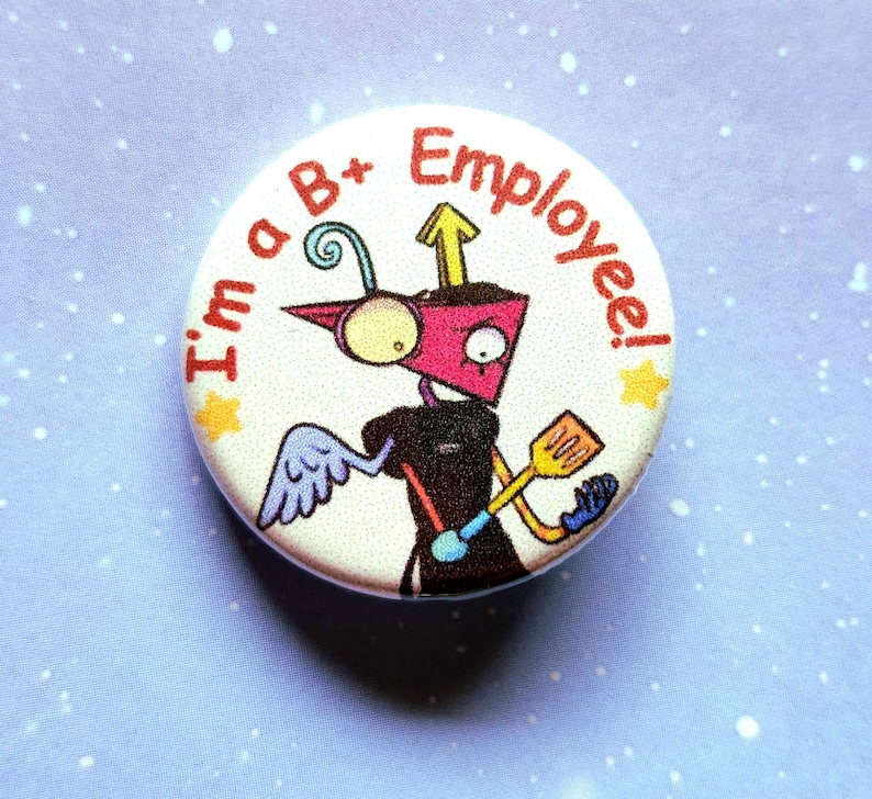 K&ouml;nnte beinhalten: Ein runder Button mit einem Cartoon-Roboter-Design. Der Roboter ist rosa, schwarz und gelb, h&auml;lt einen Spatel und tr&auml;gt einen Fl&uuml;gel. Der Text "I'm a B+ Employee!" ist am Rand aufgedruckt.