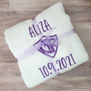 May include: White towel with purple embroidery. The embroidery includes the name "Aliza", a shield with the letters "CR" inside, and the date "10.9.2021".