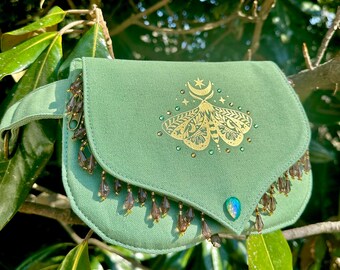 May include: A green canvas fanny pack with a gold moth design and beaded fringe. The moth has a crescent moon and stars above it.