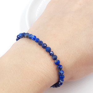 Pode incluir: Um bracelete de pedras azuis feito com contas de lapis-lazúli facetadas.