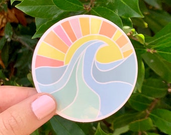 May include: A round sticker with a colorful sun and a blue wave. The sun is a gradient of pink, orange, and yellow. The wave is a gradient of blue and green.