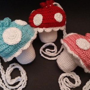 May include: Three crocheted mushroom-shaped purses with white straps. The mushrooms are in blue, red, and pink.