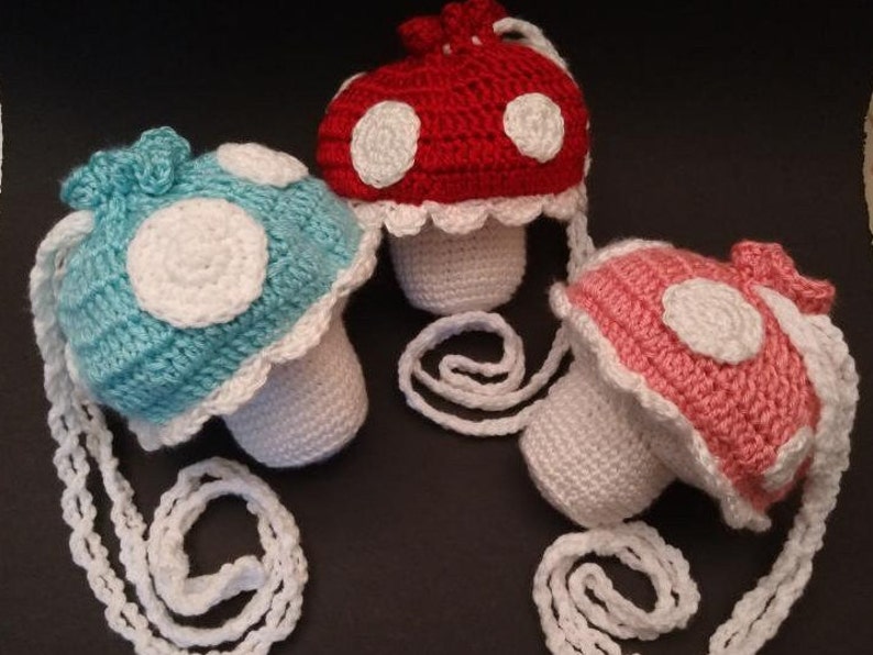 May include: Three crocheted mushroom-shaped purses with white straps. The mushrooms are in blue, red, and pink.