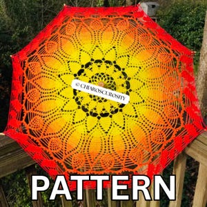 Può includere: Un ombrellino all'uncinetto caratterizzato da una vivace sfumatura di colore che passa da un centro giallo brillante a un bordo esterno arancione e rosso intenso. L'intricato design in pizzo mostra un motivo a mandala radiale.